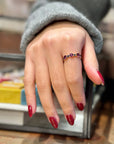 Hand with red nail polish wearing a gold ring set with multicolored gemstones