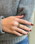 Hand wearing gold ring with green and white gemstones, cozy sweater background