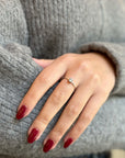 Hand with red nails wearing a delicate gold ring with a round diamond on a grey sweater